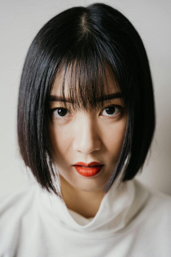 A striking close-up portrait of a woman with red lipstick and short hair, wearing a white shirt.