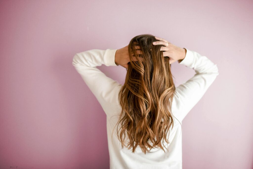 pexels-photo-973401-973401 Back view of a woman with elegant long brown hair against a pink wall, showcasing stylish hair design.